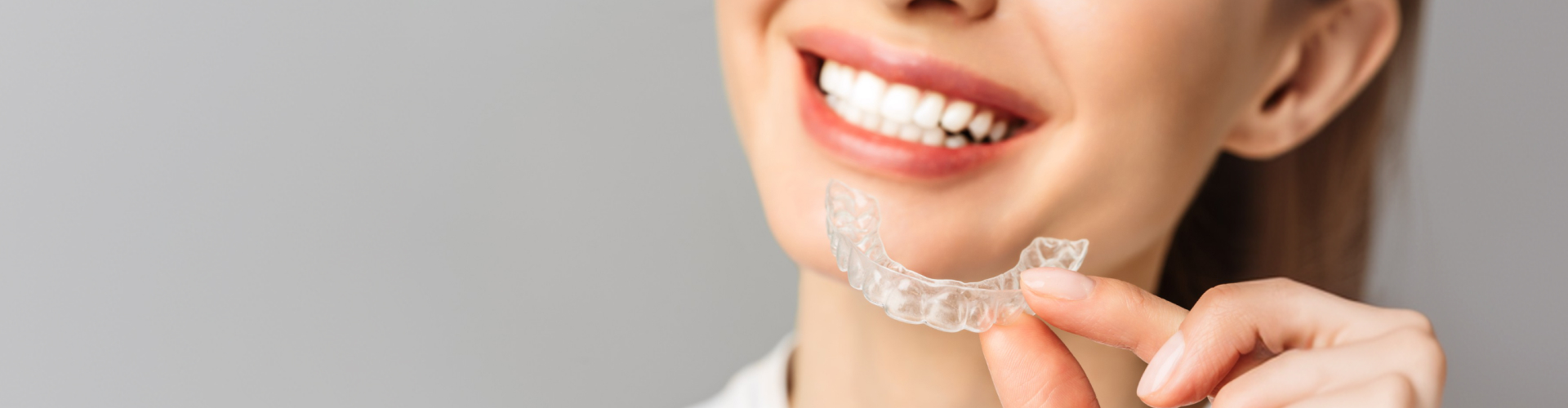 Close-up of a smiling person holding a clear aligner tray in front of their teeth, highlighting discreet orthodontic treatment with removable clear aligners.